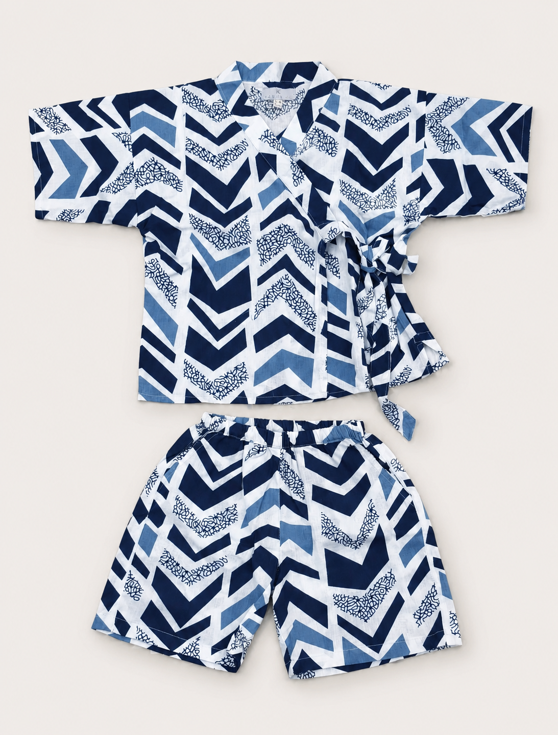 A two-piece baby outfit set consisting of a short-sleeve wrap shirt and matching shorts, both featuring a blue, navy, and white chevron pattern on a light beige background.