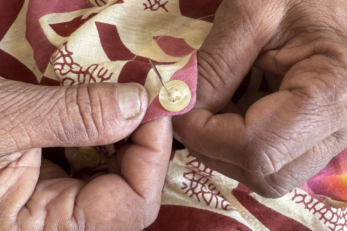Close-up of hands stitching a button onto a block-printed cotton kurta by hand