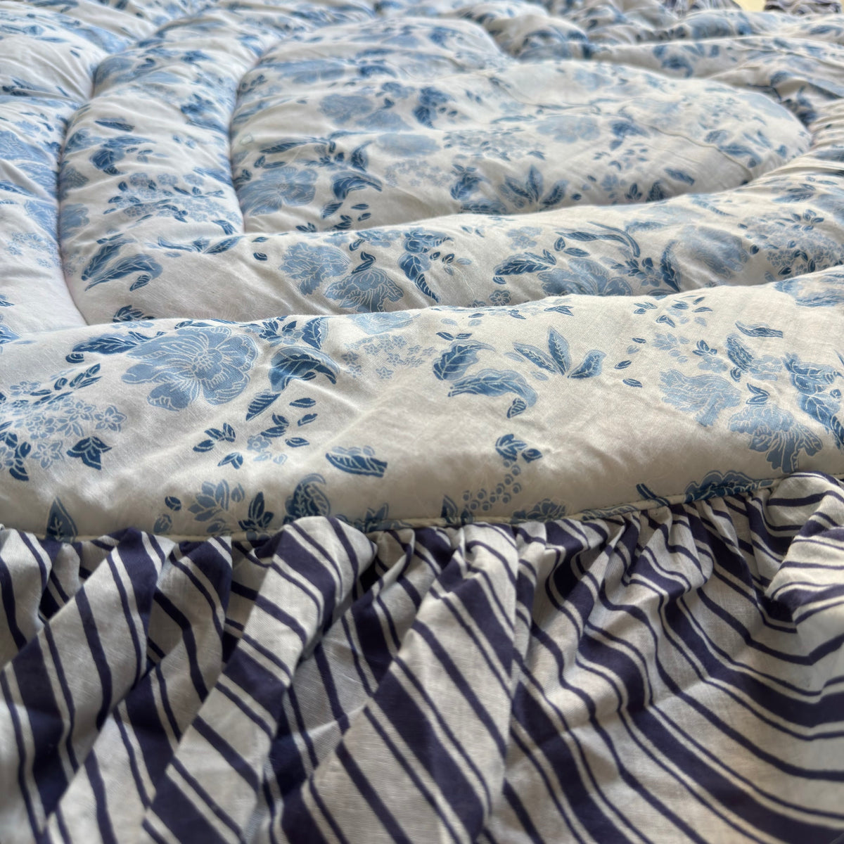 Side close-up of the blue floral mat showing the padded quilting and navy striped ruffle